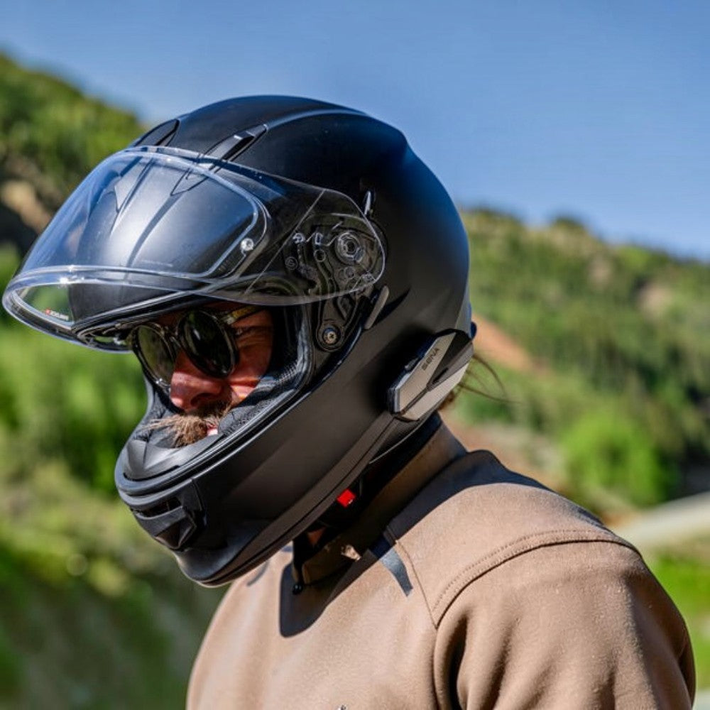 Moto Explorer Sena 60X Bluetooth communication system mounted on a matte black motorcycle helmet worn by a rider.